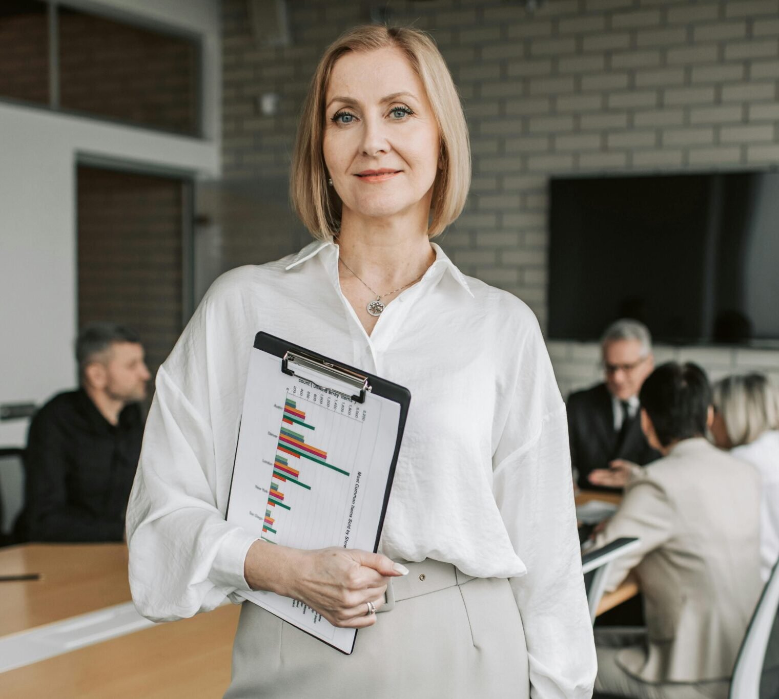 Professional businesswoman holding a clipboard during an office meeting, showcasing leadership in a corporate environment.